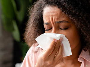 Image of a woman sneezing into a tissue
