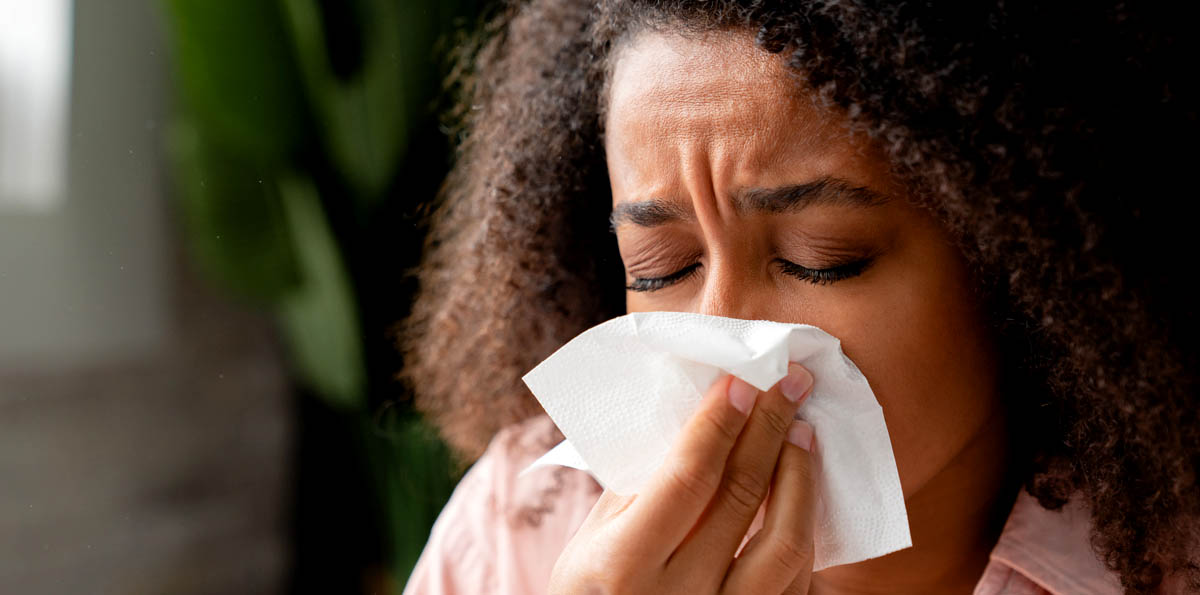 Image of a woman sneezing into a tissue.